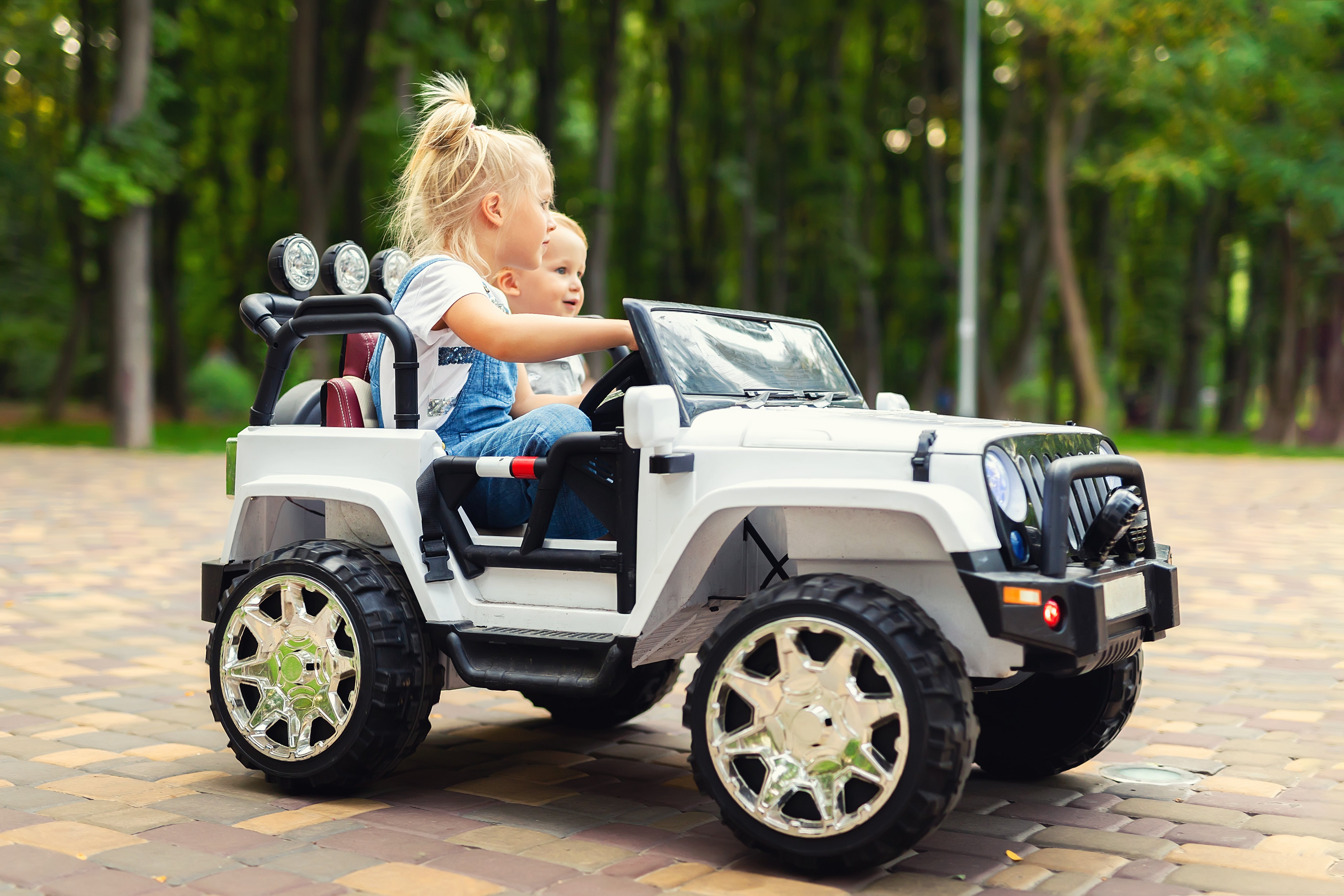 Ein Mädchen und ein Junge sitzen auf ein weißes Spielauto.