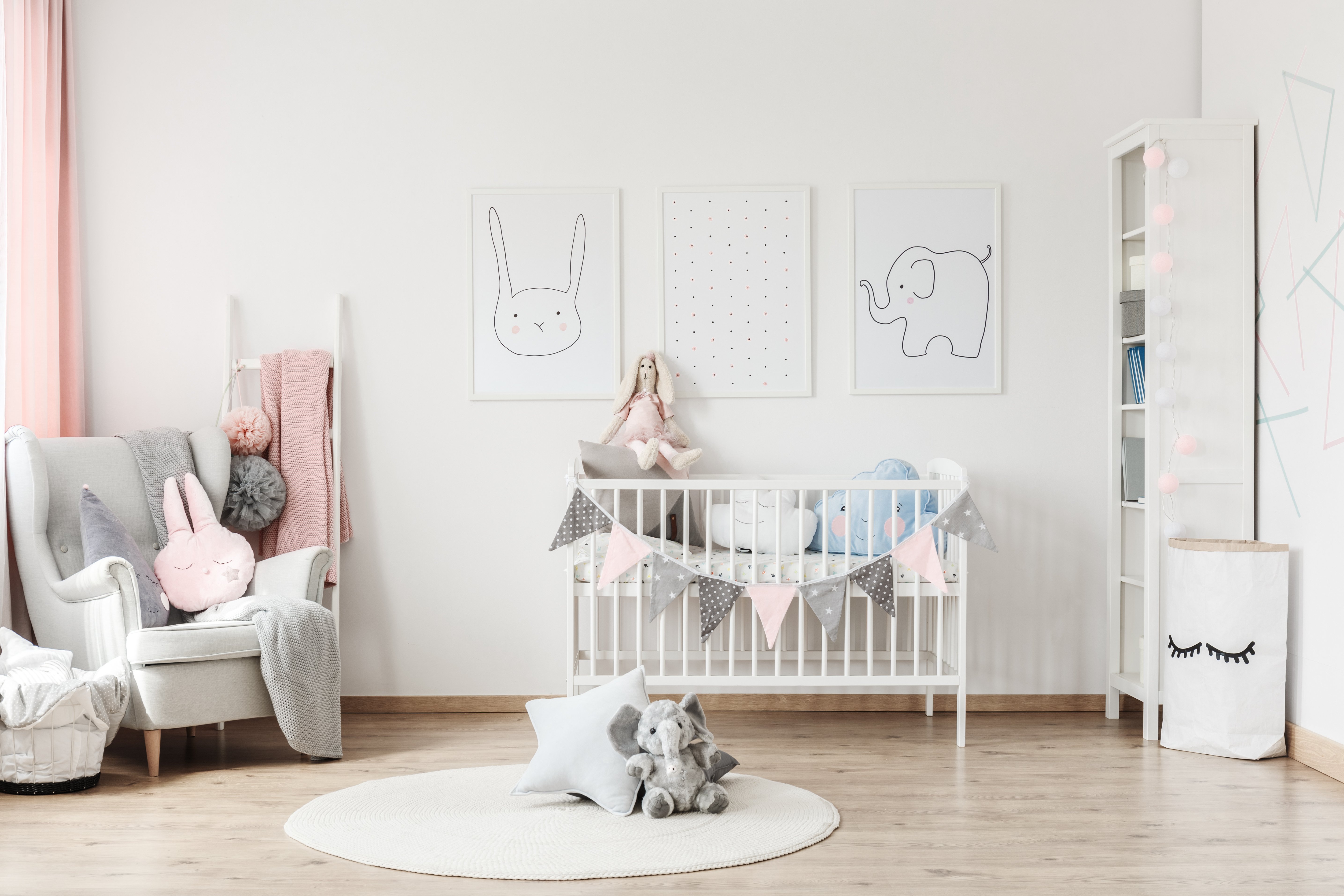 In einem Kinderzimmer befindet sich ein weißes Kinderbett, ein Ohrensessel, ein Regal und ein runder weißer Teppich.
