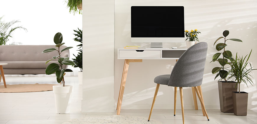 Kleiner Schreibtisch mit Computer und Stuhl vor einer weißen Wand