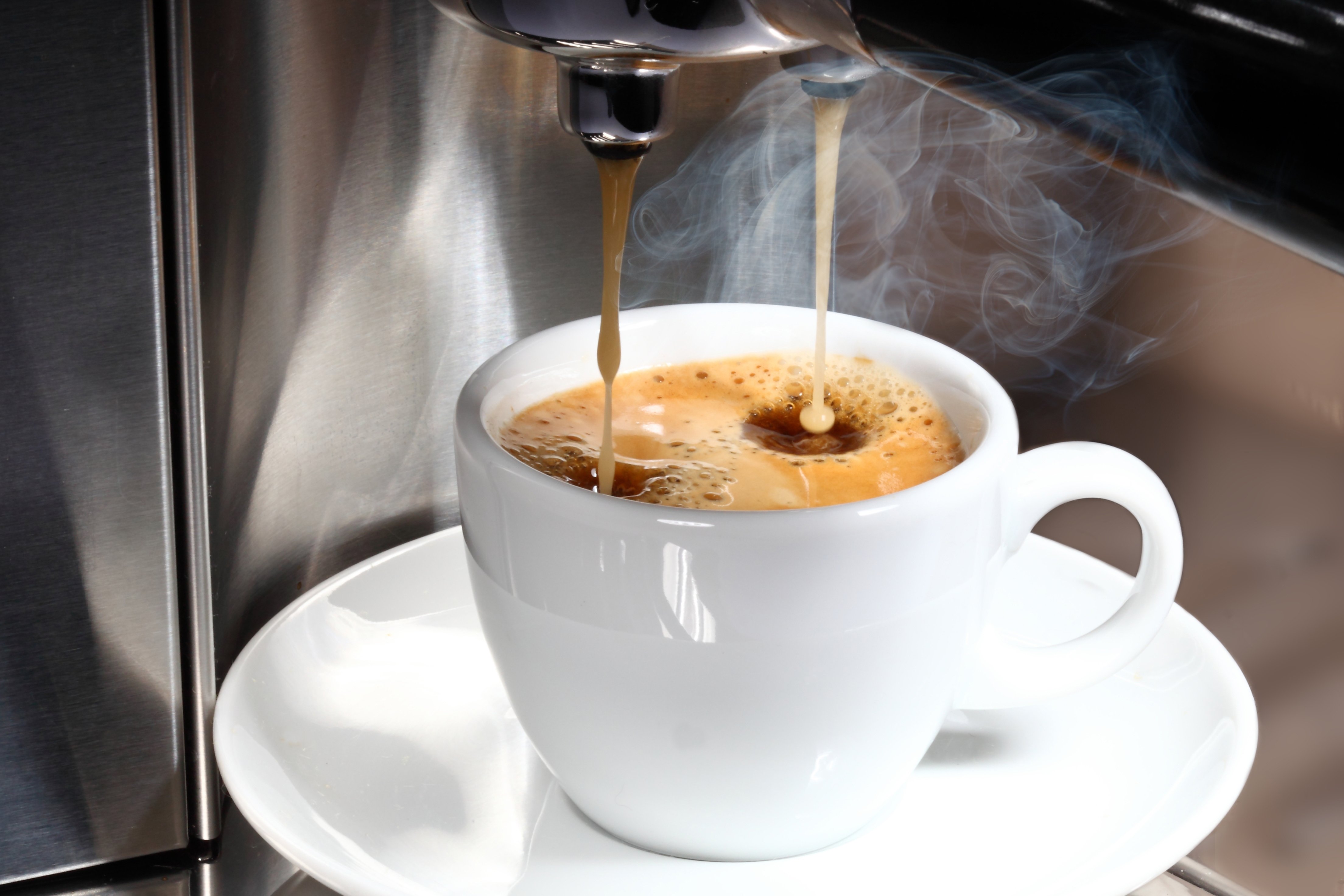 Eine Kaffeemaschine gießt frisch gebrühten Kaffee in eine weiße Kaffeetasse.