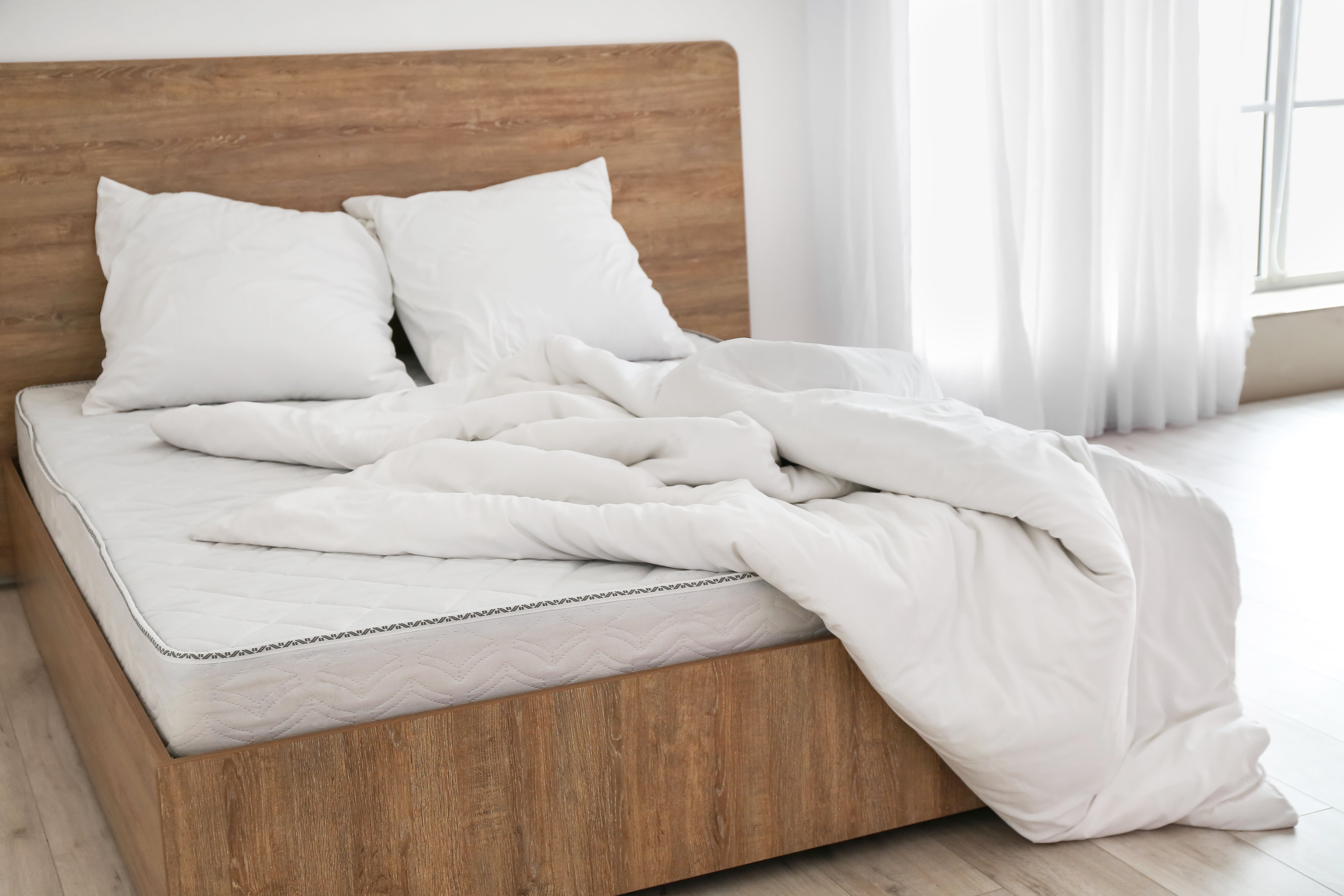 Auf einem Bett liegt eine weiße Matratze, zwei weiße Kissen und eine weiße Daunendecke.